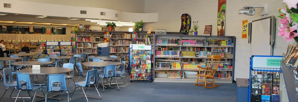 St. Elizabeth Seton Catholic School library with rows of books, tables and chairs and a rocking chair in the right corner.